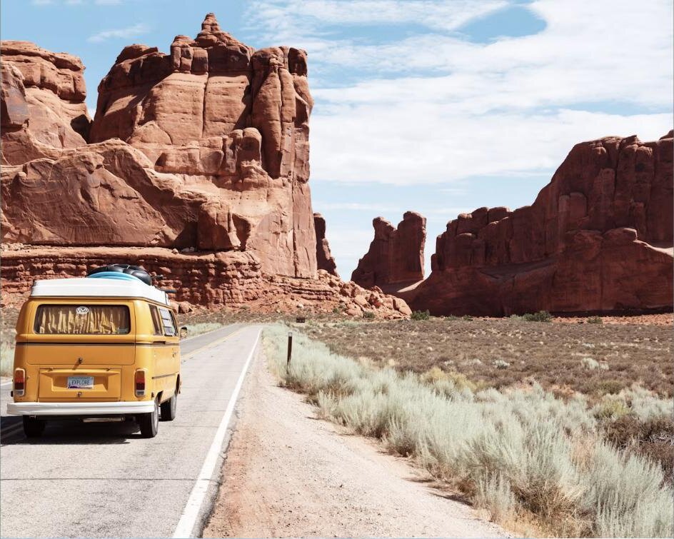 Yellow campervan driving through a red rock desert landscape