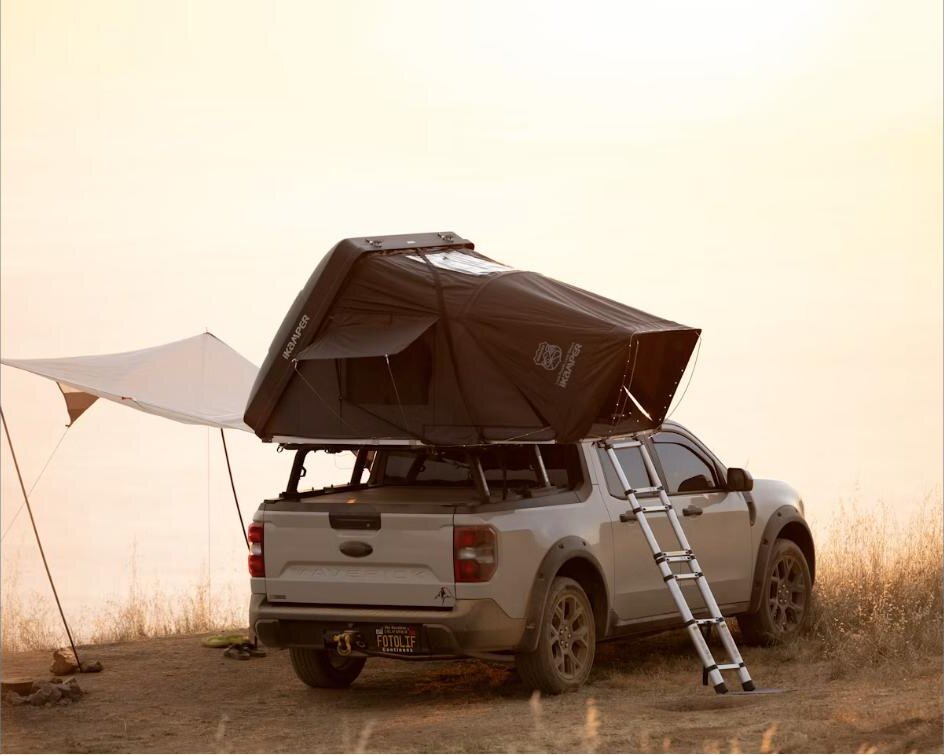 Pickup truck with a rooftop tent set up at a sunset campsite by the water